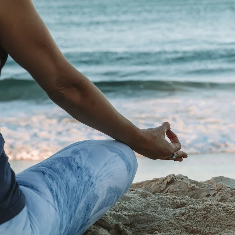 A woman sitting in the sand at the ocean doing yoga.