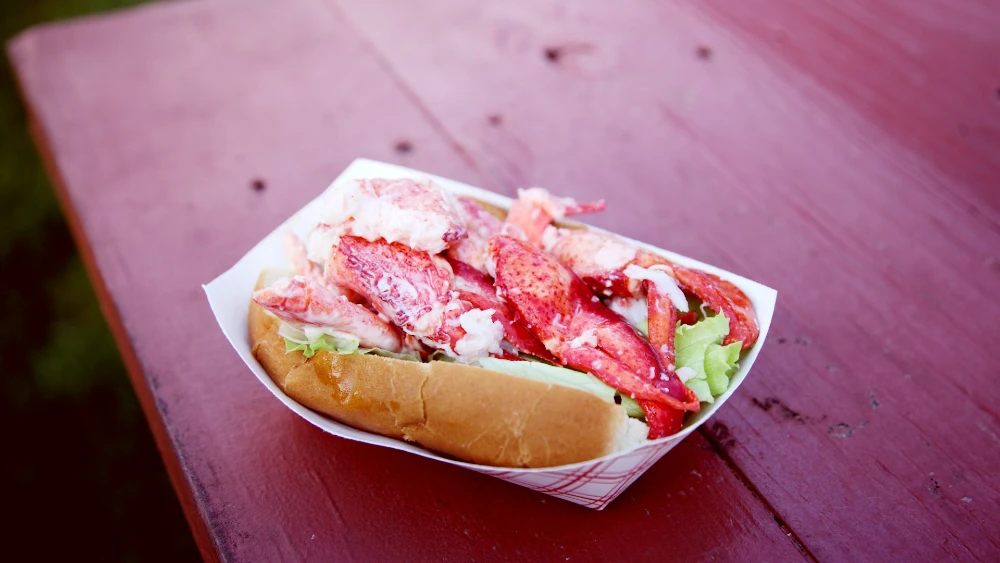 A lobster roll sitting on a picnic table.