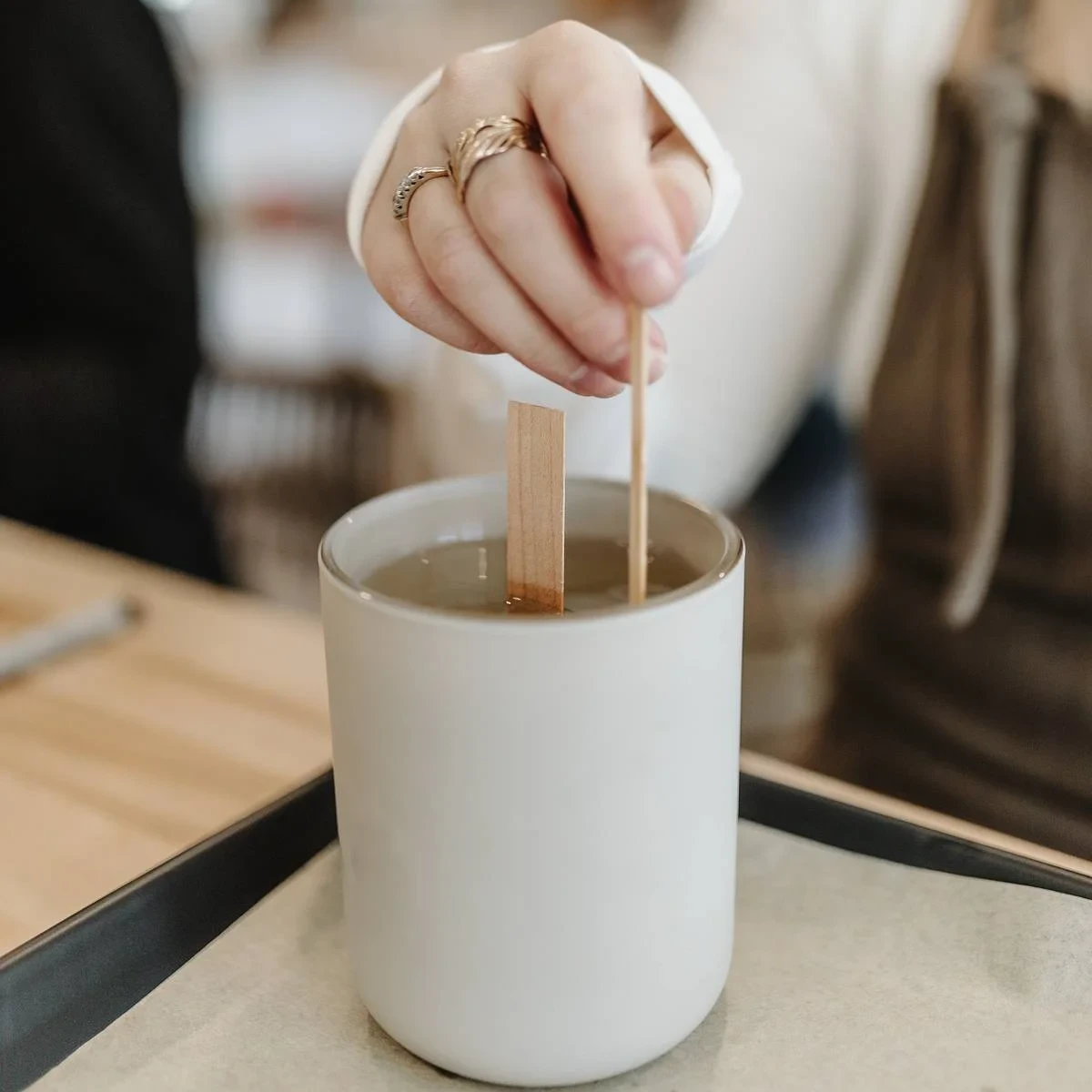 A woman's hand dipping a candle wick into hot wax.