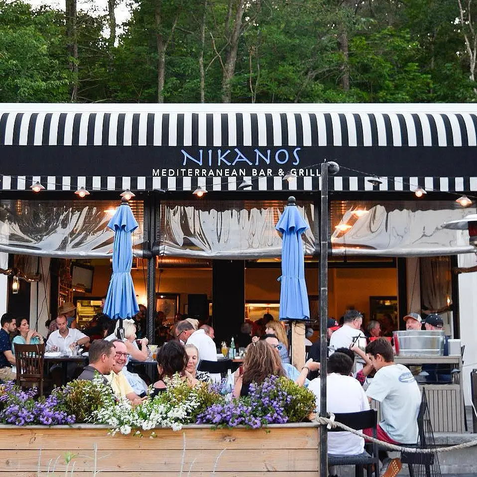 People sitting at dining tables outside at the Nikanos restaurant.