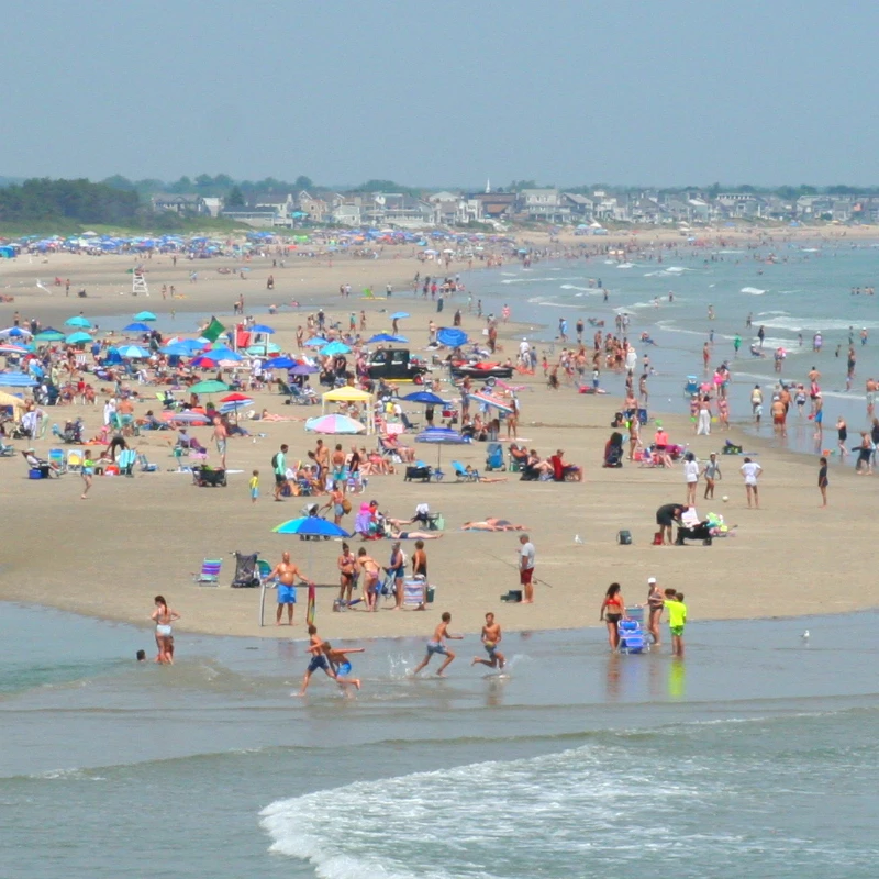 A view of Ogunquit beach from a distance, the beach is filled with colorful umbrellas and people sunbathing and playing.