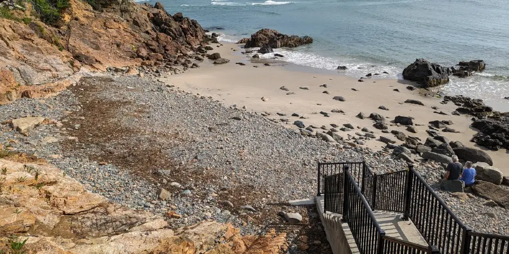 Stairs lead down to a small beach with two people sitting on a rock