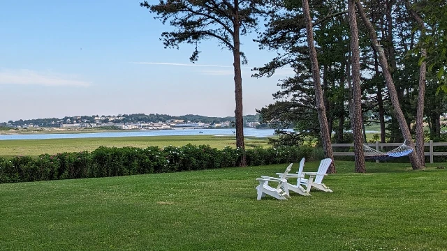 White adirondack chairs and a hammock on a grassy yard facing the Ogunquit river.